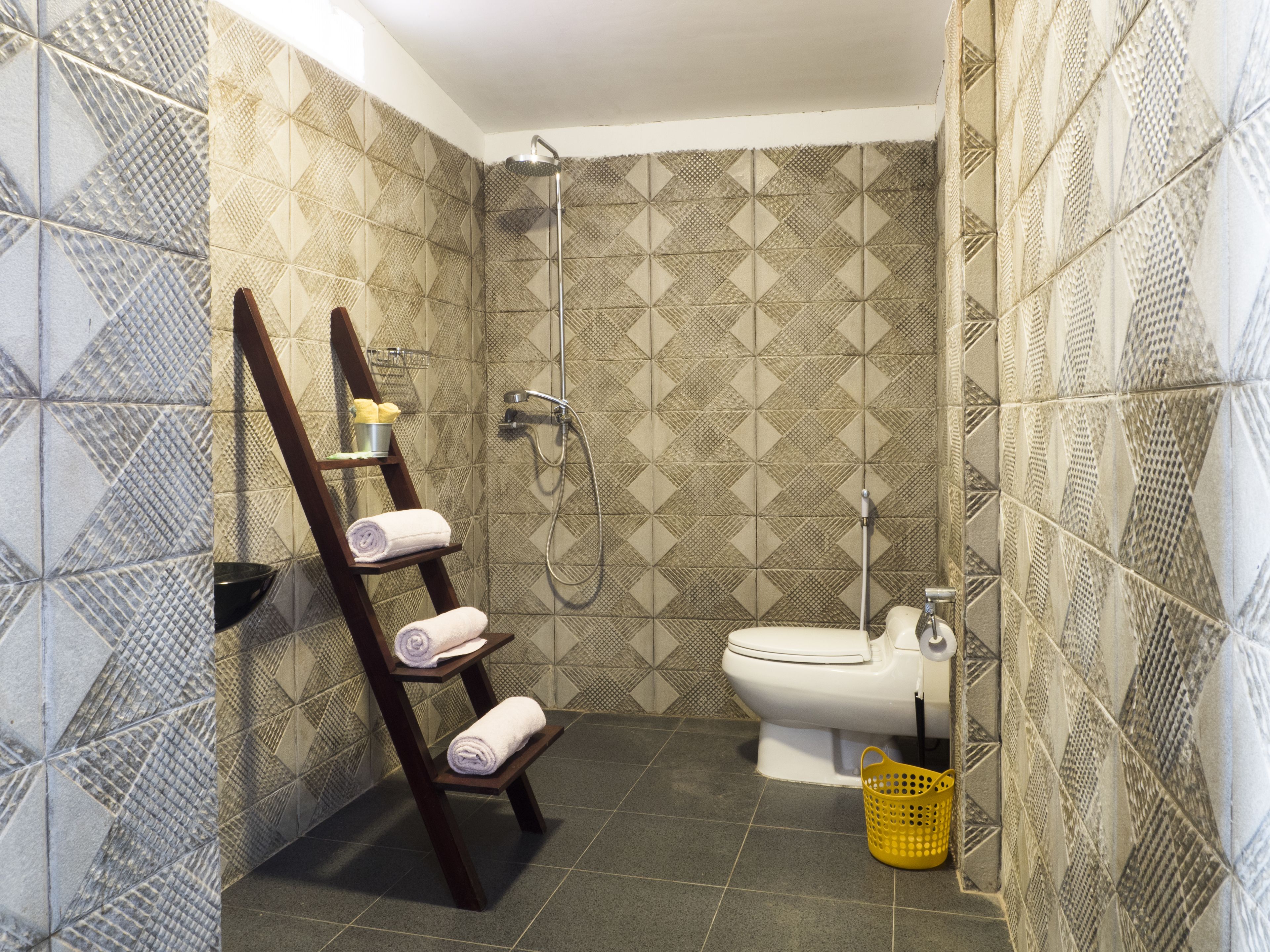 A bathroom with patterned tiles, a wooden towel rack with towels, a toilet, and a shower.