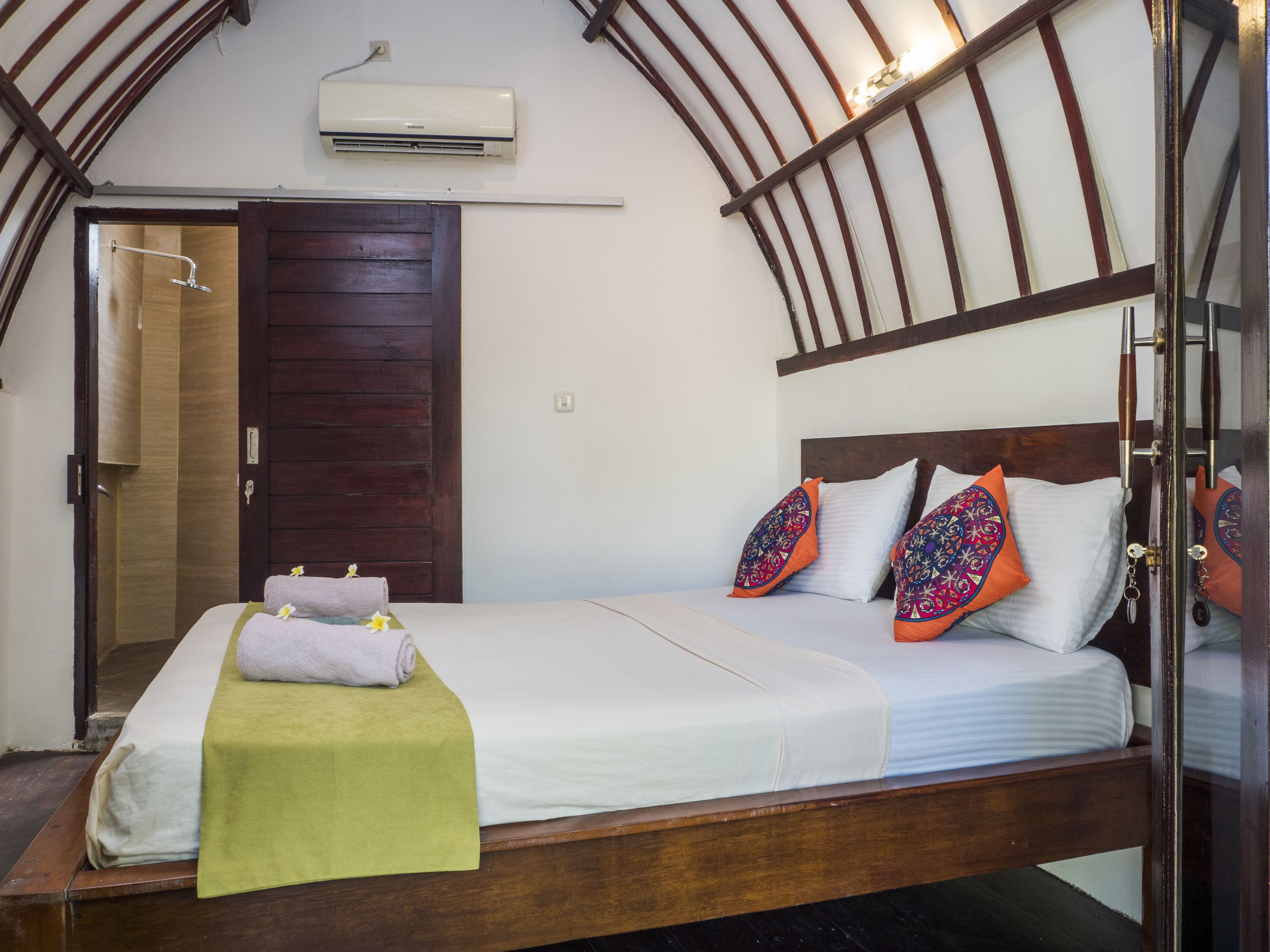Un dormitorio con estructura de cama de madera, ropa de cama blanca y almohadas coloridas.