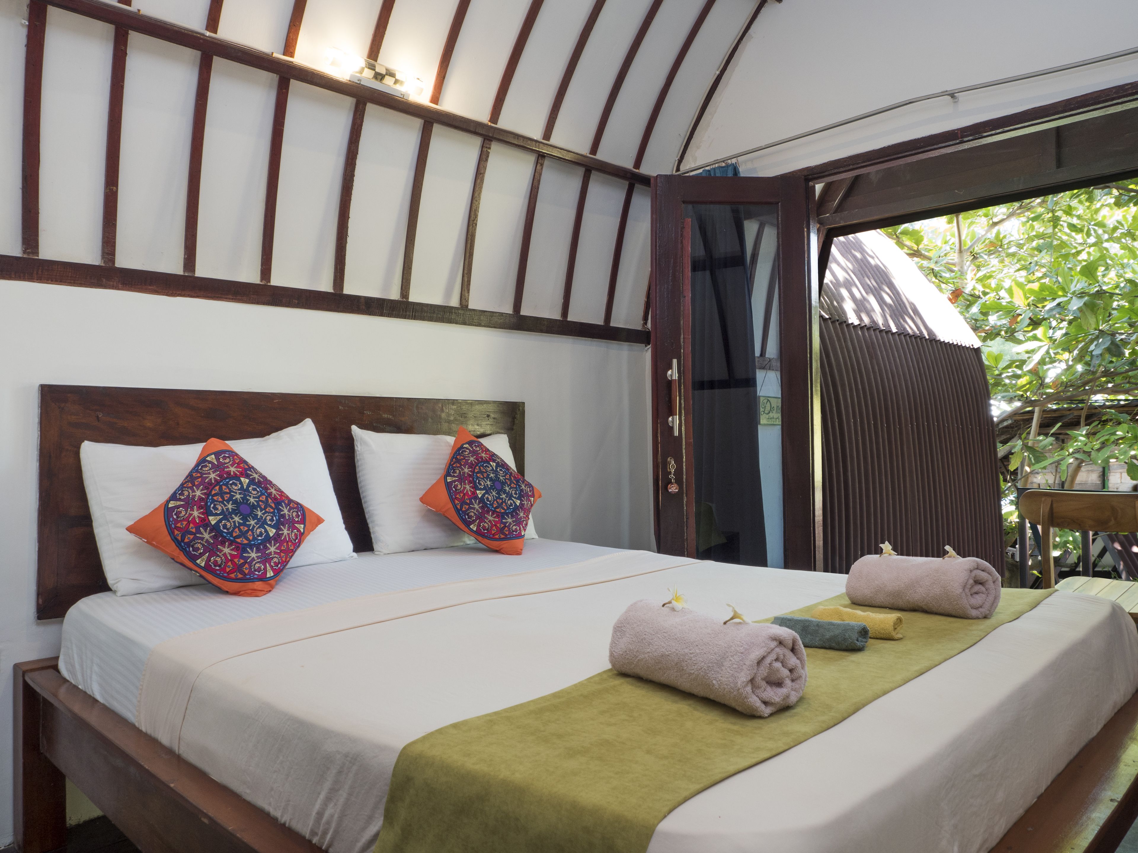 A bed with white linens, two decorative pillows, and a green towel.