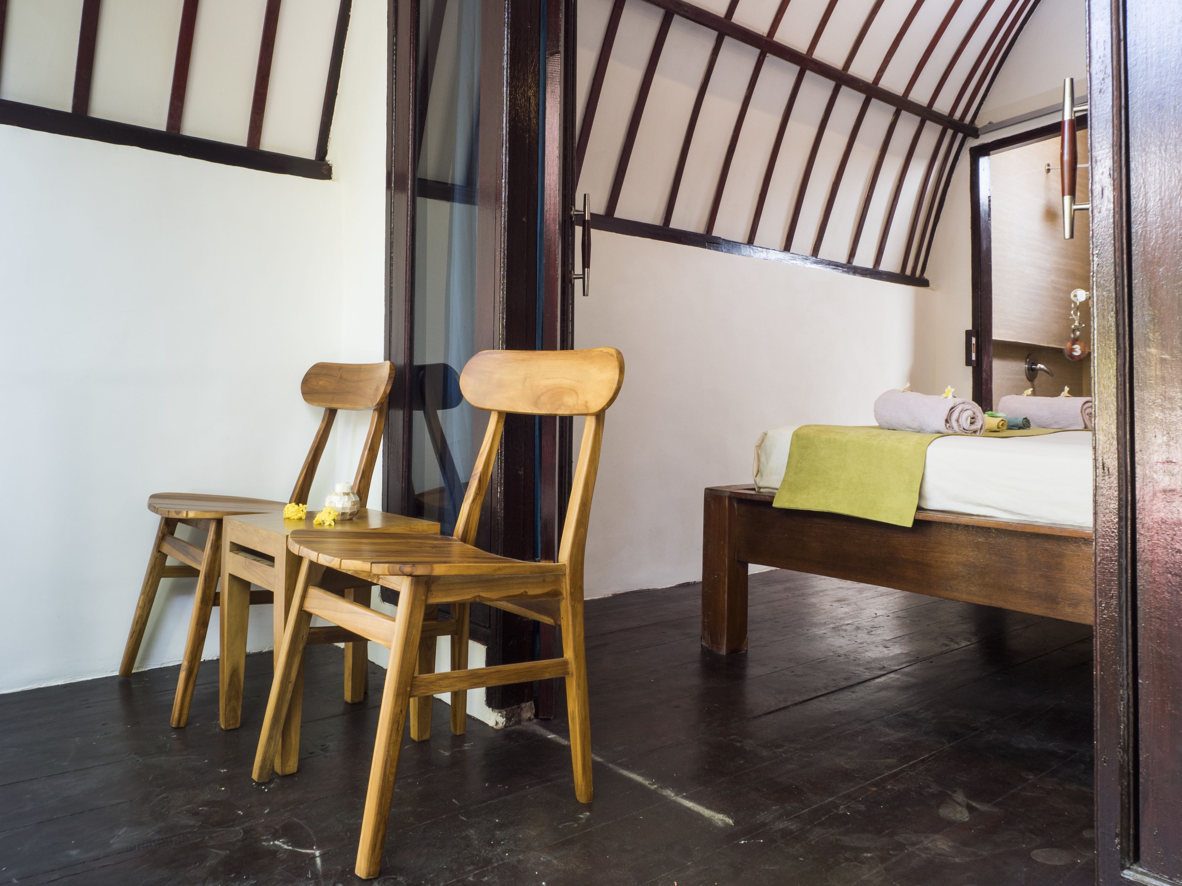 A room with a bed, two wooden chairs, and a small table.