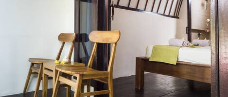 A room with a bed, two wooden chairs, and a small table.
