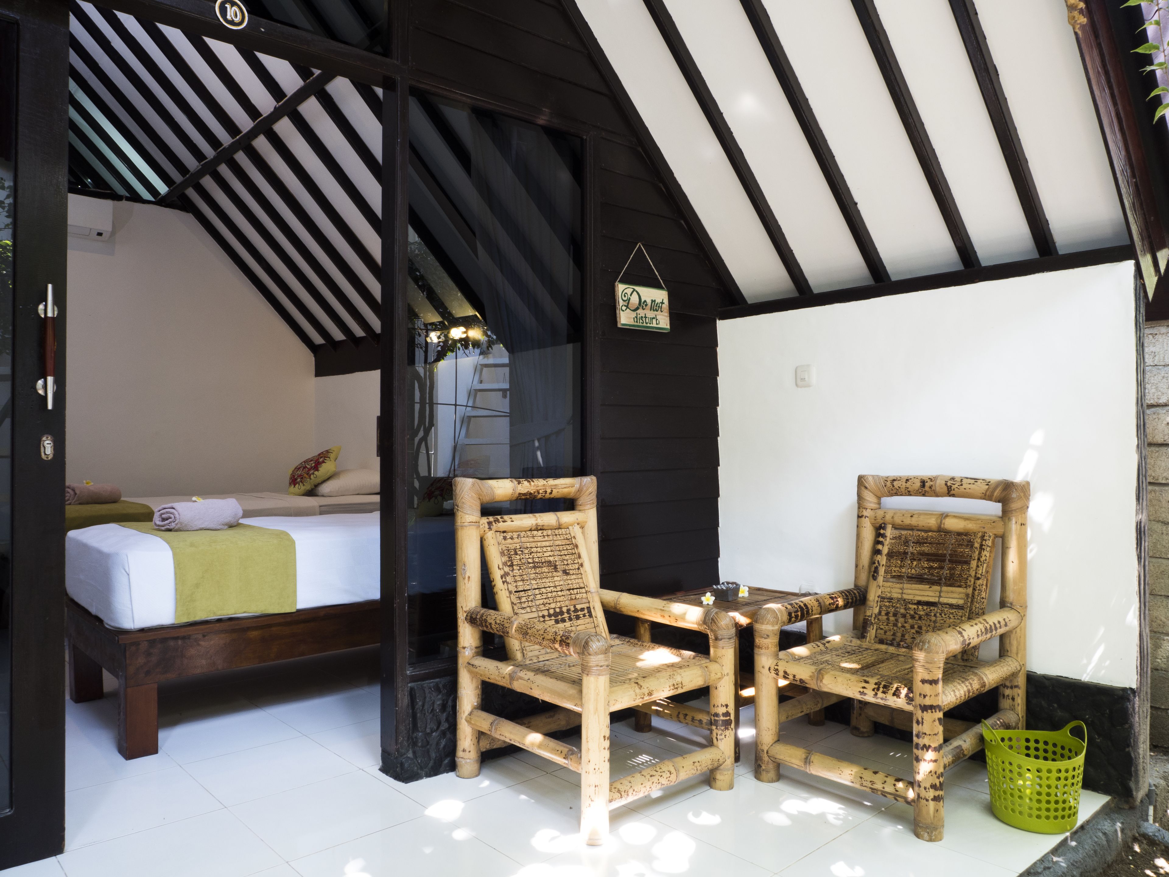 A room with a bed, two wicker chairs, a small table, and a green basket.