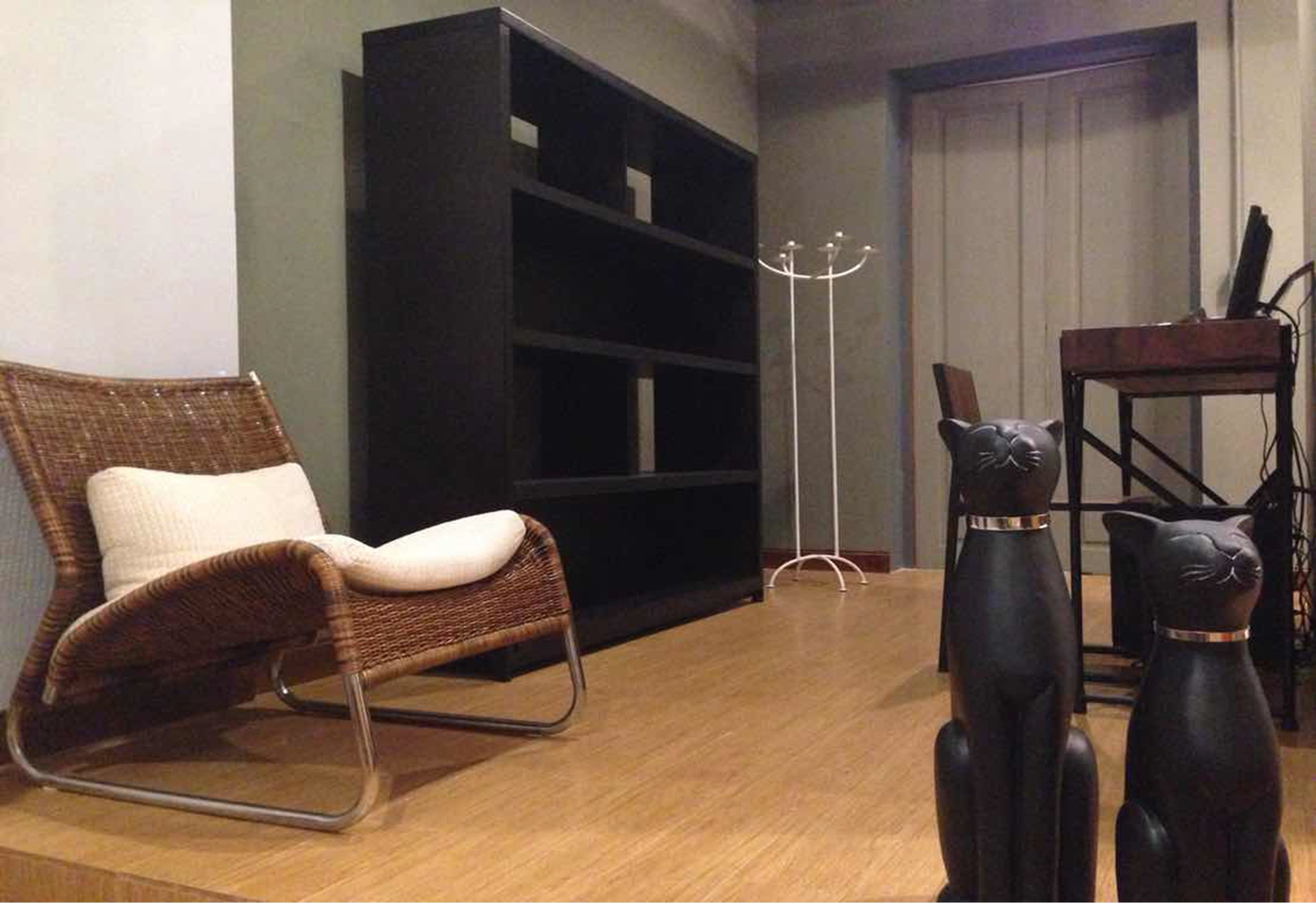 Une pièce comprenant un fauteuil en osier, une bibliothèque noire et deux sculptures de chats noirs.