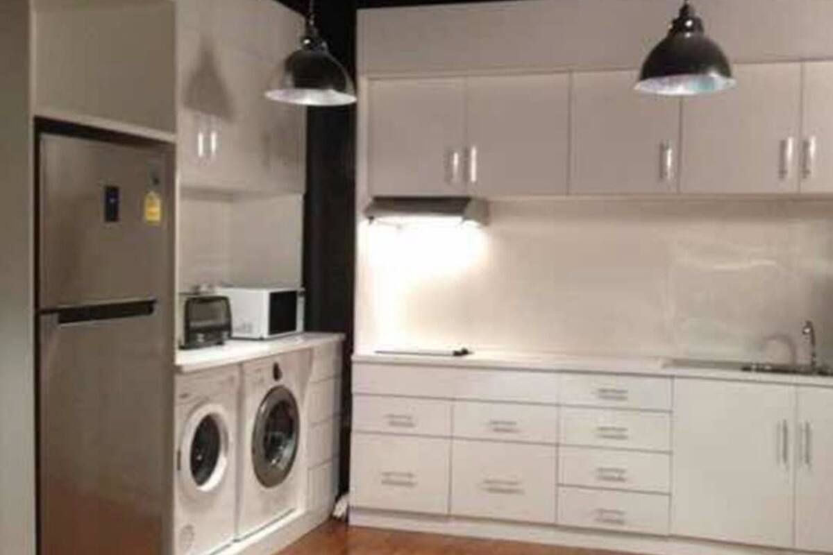 Une cuisine compacte dotée d’appareils électroménagers intégrés, de meubles blancs et d’un éclairage suspendu.