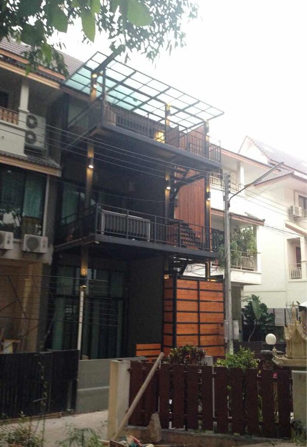 Un immeuble résidentiel à plusieurs étages, doté d’un balcon en verre à l’étage supérieur, d’une clôture en bois à l’avant et d’un lampadaire situé à proximité.