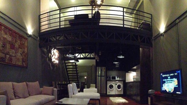 Una sala de estar moderna con sofá, mesa de centro, televisor y zona de cocina con electrodomésticos.