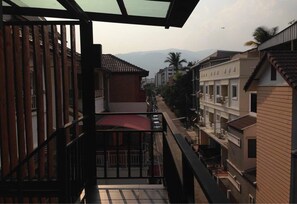 Une vue depuis un balcon doté d’une balustrade en verre, donnant sur une rue bordée d’immeubles, avec des montagnes en arrière-plan.