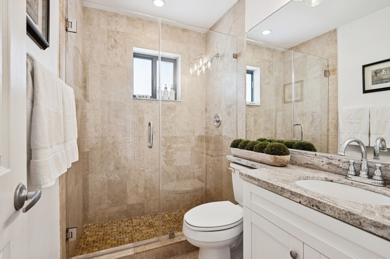 A modern bathroom with a glass-enclosed shower, a white toilet, and a vanity with a marble countertop.