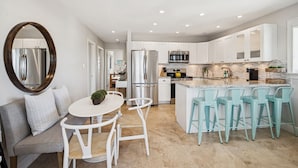 Une cuisine moderne avec des meubles blancs, des appareils en acier inoxydable et un îlot central doté de tabourets de bar.