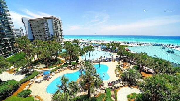 Ein Resort mit großzügigem Poolbereich, Palmen und einem Strand.