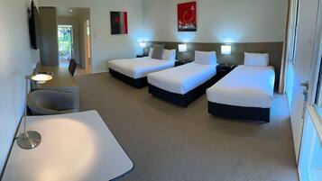 Habitación de hotel con dos camas individuales, un escritorio y una silla. Se ve una ventana a la derecha.