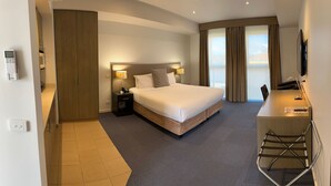 A hotel room with a large bed, bedside tables, a desk with a chair, and a view of the outdoors. - Brooklands of Mornington (Mornington)