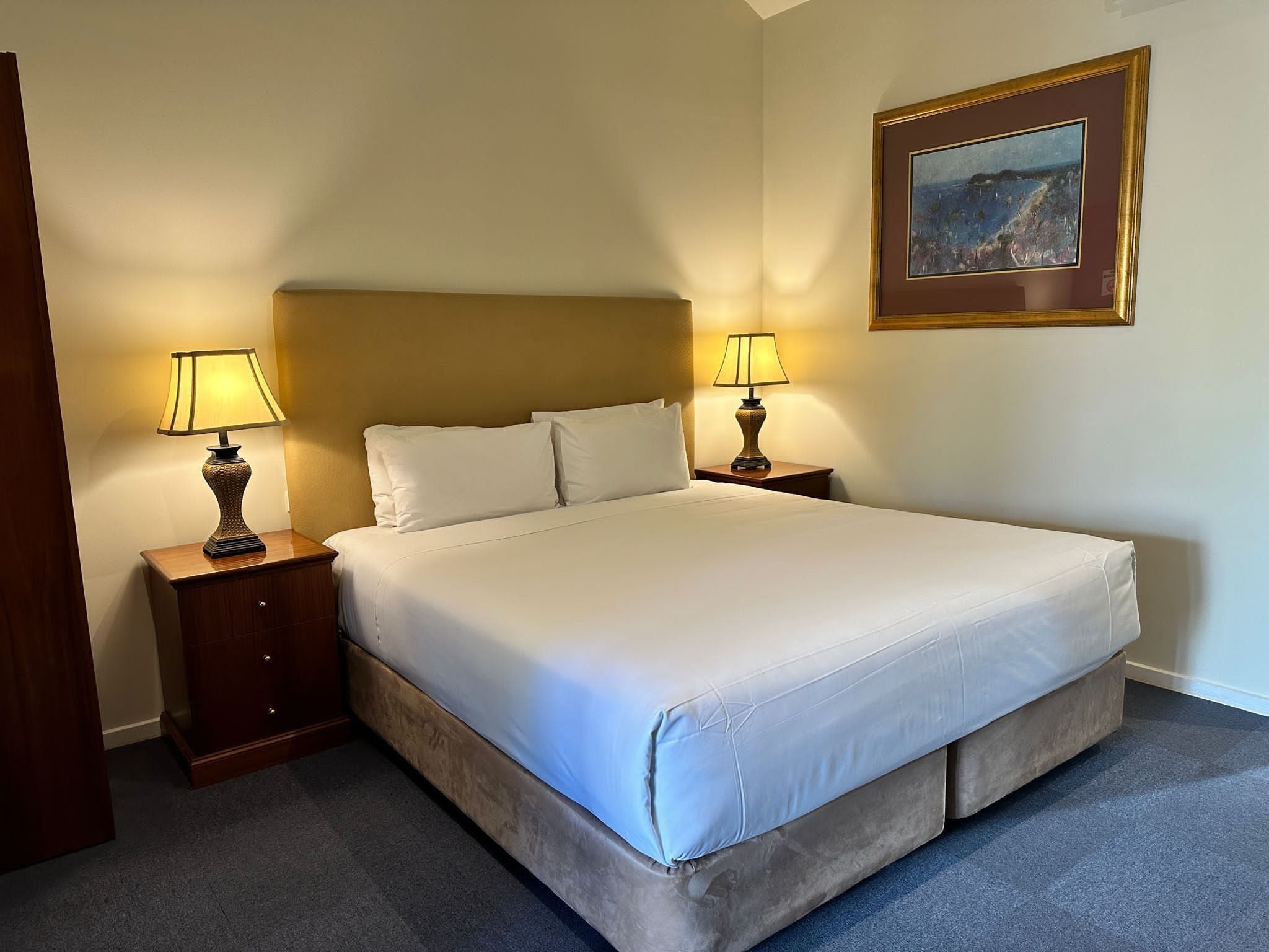 A neatly made bed with white linens and two bedside lamps.