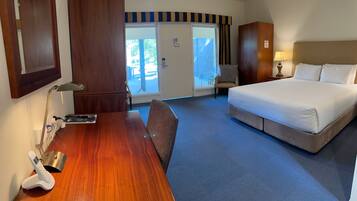Habitación de hotel con cama, escritorio con teléfono, una silla, lámpara y vistas al exterior.