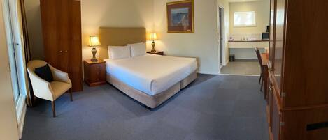 A hotel room with a large bed, a chair, a desk, and a bathroom visible through an open door.