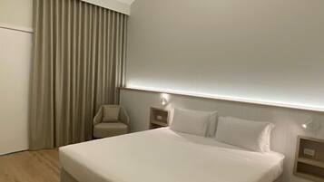 Una habitación de hotel moderna con una cama grande, una silla, una mesita de noche y un estante empotrado.