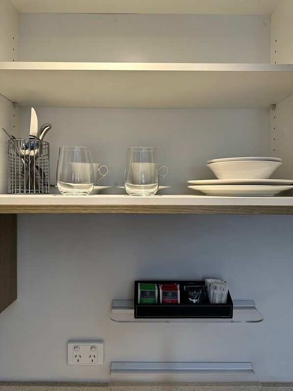 Una repisa de cocina con un organizador para cuchillos, dos vasos y una pila de platos.