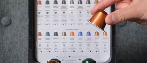 A hand selecting a Nespresso capsule from a display case.