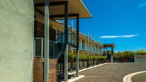 A modern hotel with a covered walkway, a parking lot, and a clear blue sky. - Brooklands of Mornington (Mornington)