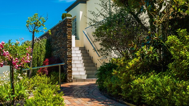 A garden pathway leading to a house with a stone wall and a staircase. - Brooklands of Mornington (Mornington)