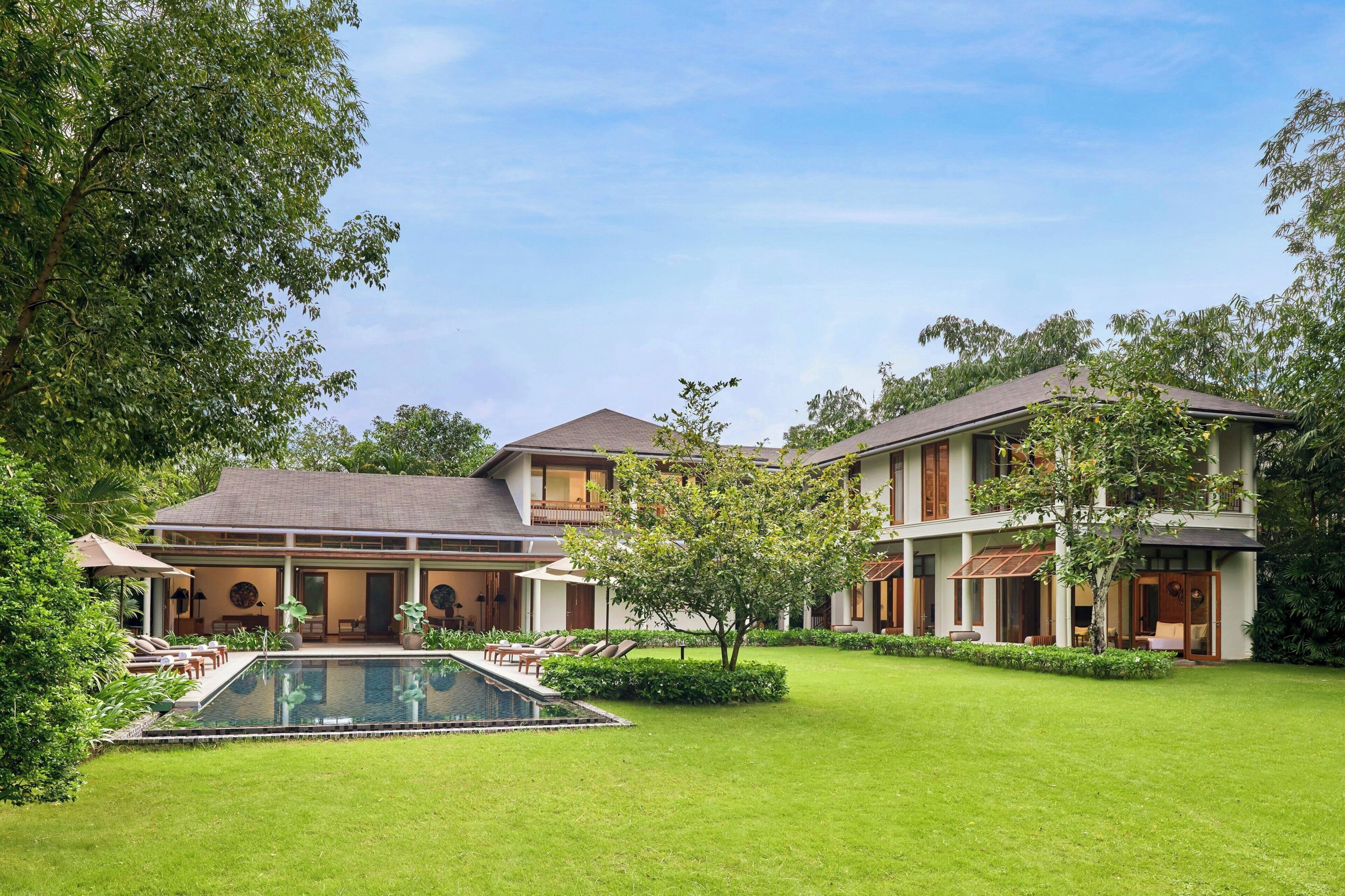 A two-story house with a swimming pool, surrounded by a well-maintained lawn and trees.