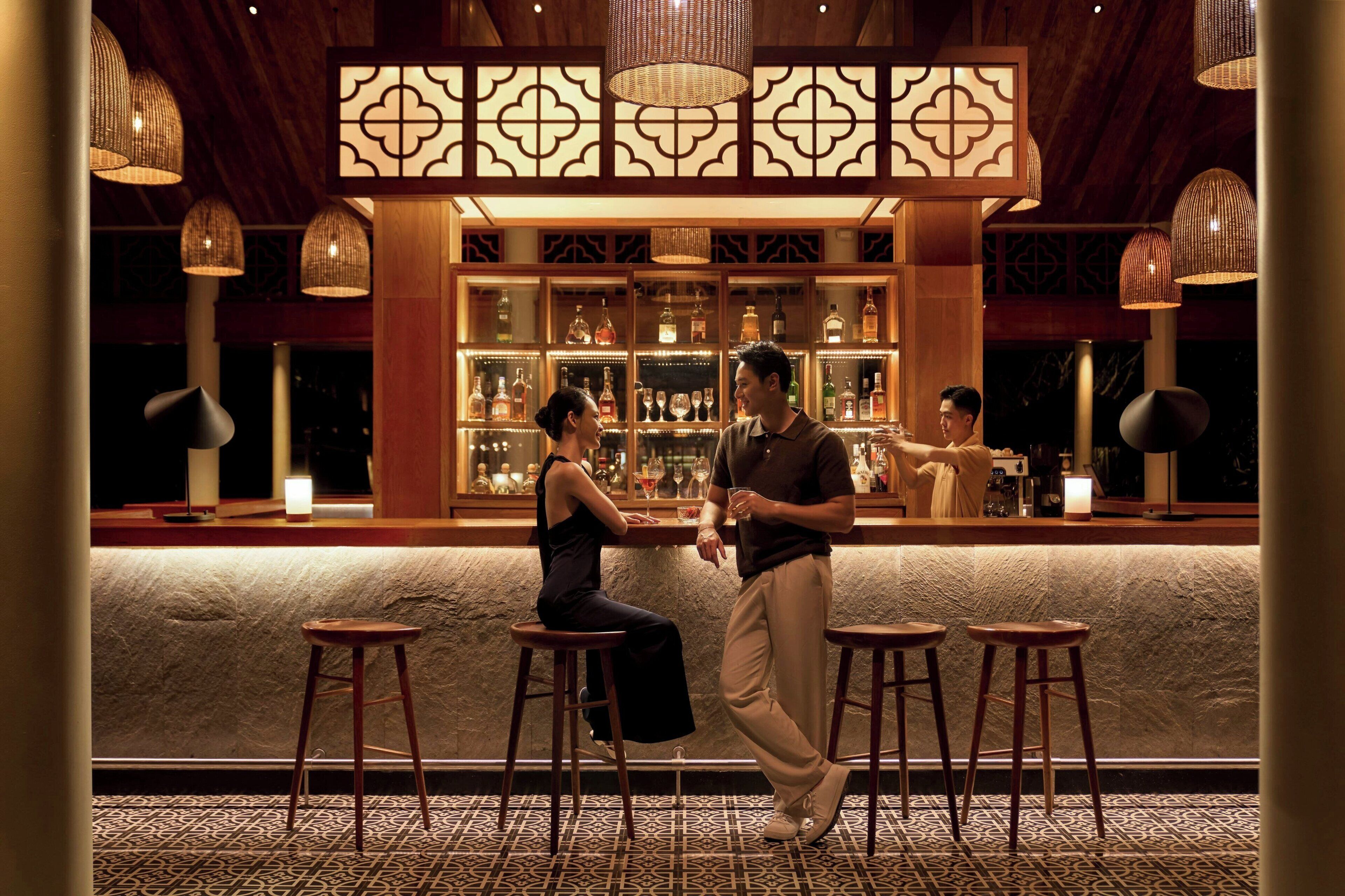 A bar area with a stone counter, wooden stools, and hanging wicker lamps.