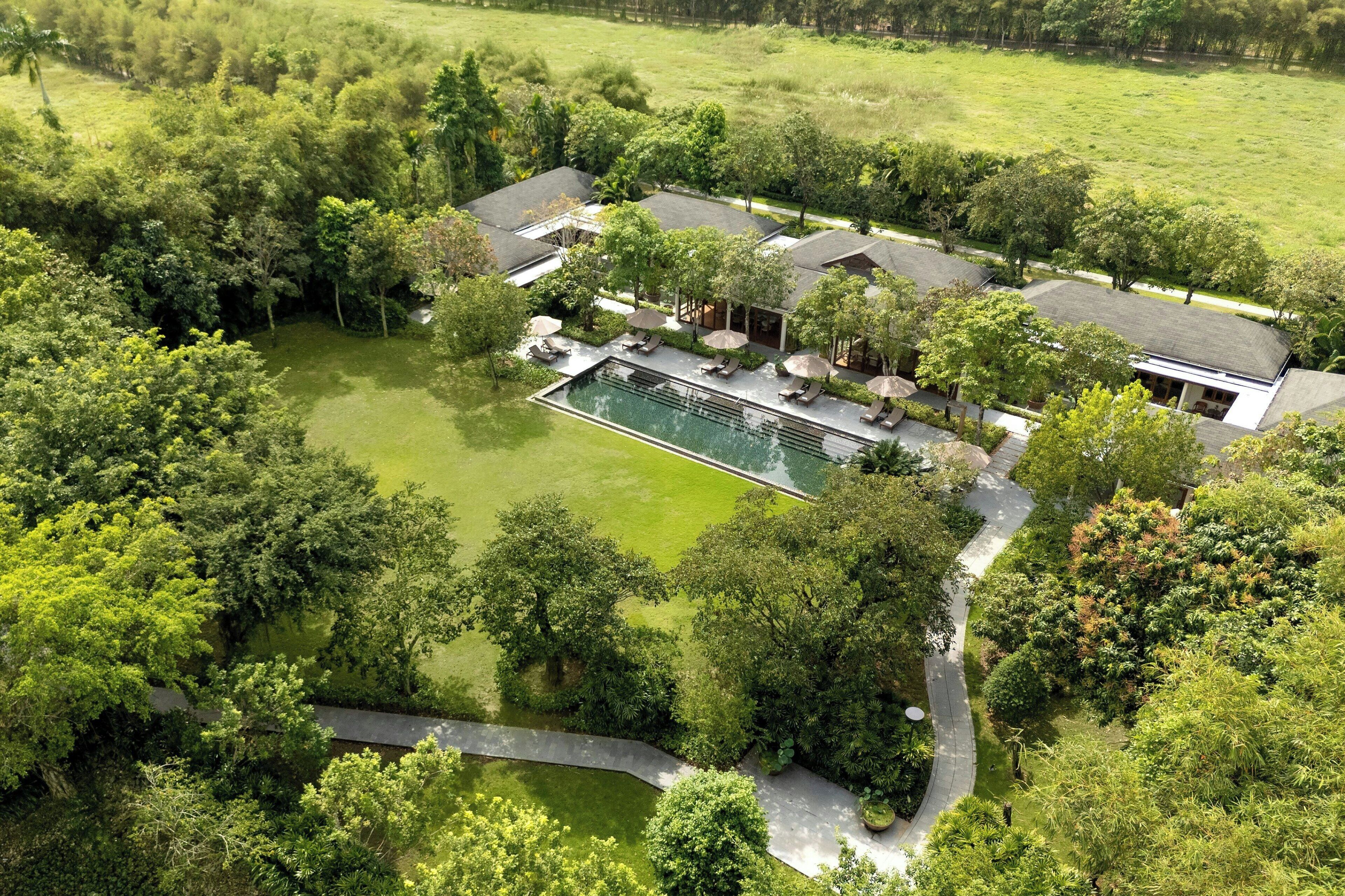 An aerial view of a resort with a swimming pool, lounge areas, and lush greenery.