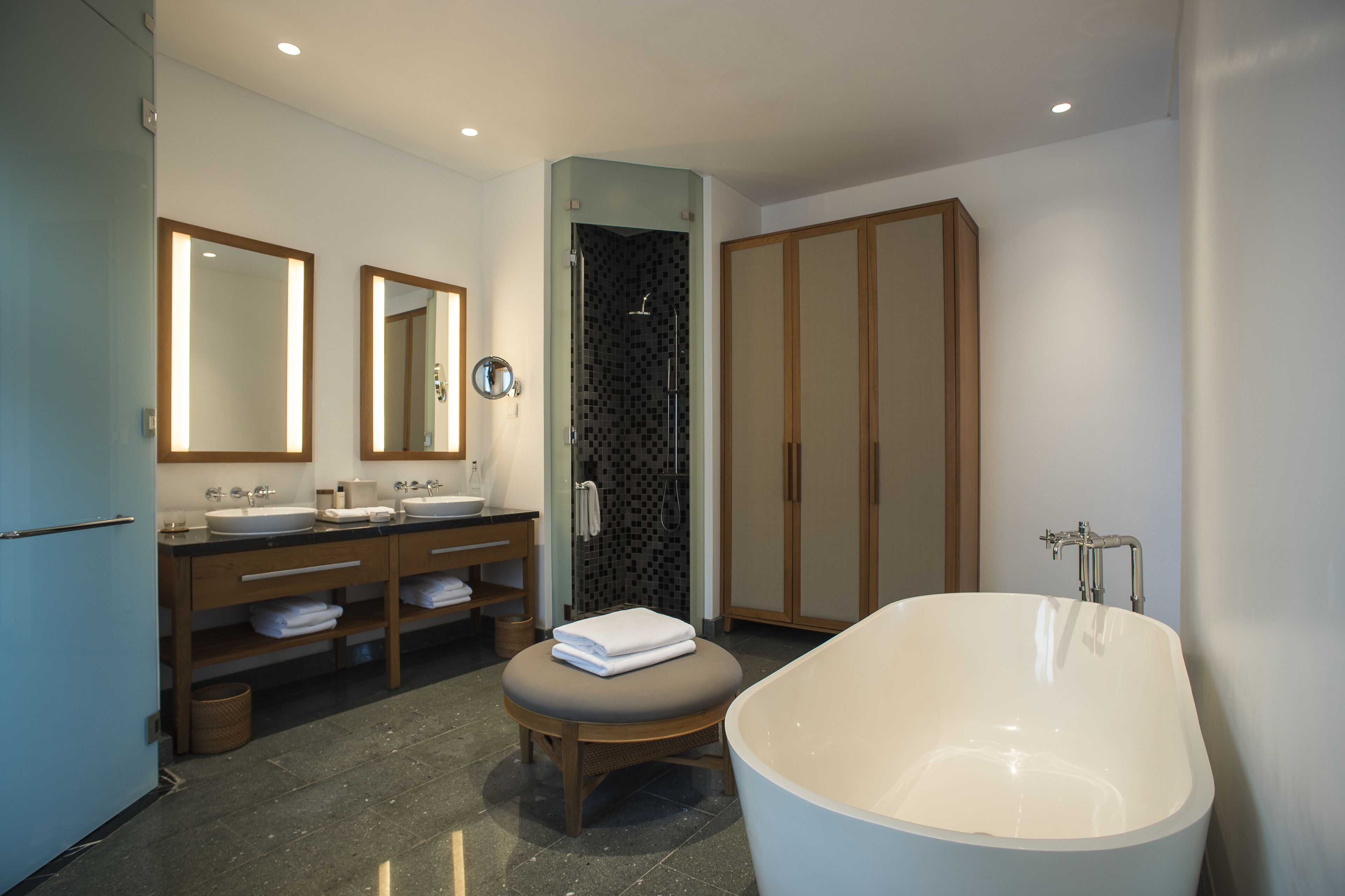 A modern bathroom with a freestanding bathtub, two sinks, a vanity with a mirror, and a walk-in shower.