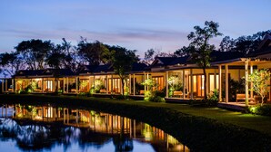 A row of modern, well-lit buildings with reflective water in the foreground, likely part of a resort or hotel. - Legacy Mekong, Can Tho, Autograph Collection (Can Tho)