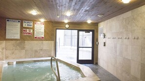 Een wellnessruimte met een whirlpool, houten plafond en betegelde muren.