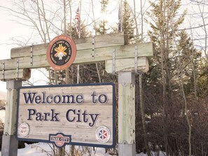 A wooden welcome sign for Park City with a maple leaf emblem and a flag.