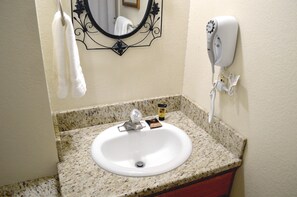 A bathroom with a granite countertop, a white sink, a hairdryer mounted on the wall, and a towel hanging on a rack.