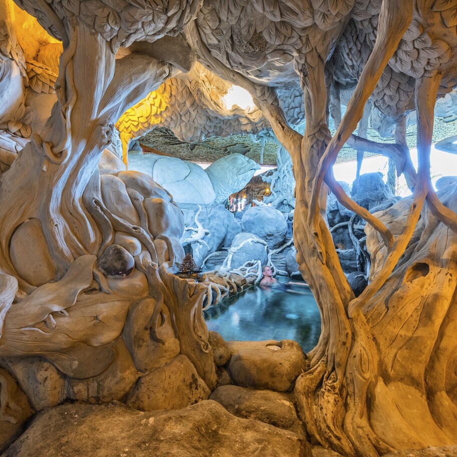 An intricate indoor tree sculpture with detailed branches and roots, a small water feature, and a view of the outside.