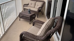 Un balcon doté de mobilier en osier, comprenant deux chaises et une petite table, et offrant une vue sur l’océan.