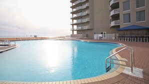 Une piscine avec un espace aménagé au bord de la piscine, un bâtiment doté de nombreux balcons et une vue sur la mer.