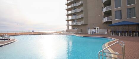 A swimming pool with a poolside area, a building with multiple balconies, and a view of the sea.