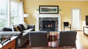 Una sala de estar con chimenea, un sofá, dos sillones, un televisor y una ventana con cortinas.