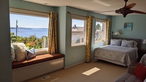 Un dormitorio con un ventanal grande, una cama, un ventilador de techo y vistas al agua.