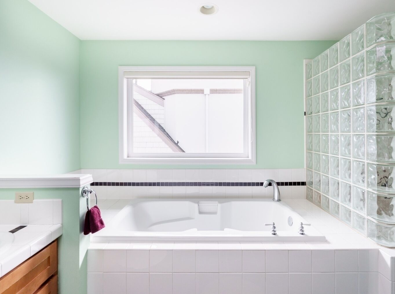 A bathroom with a bathtub, a window, and a tiled wall.