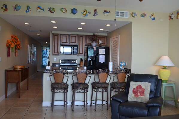 A kitchen with a central island, bar stools, and a dining area with a black leather chair and a lamp. - Splash luxury Beachfront Condo on 7th flr. Waterpark, Beach Service, Ocean views (Panama City Beach)