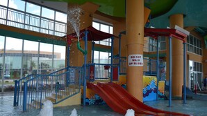 An indoor water park with a red slide, multiple water jets, and a 'Do Not Walk Up Slides' sign.