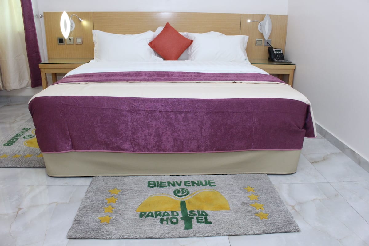 A hotel room with a bed, a nightstand, a phone, and a welcome mat.