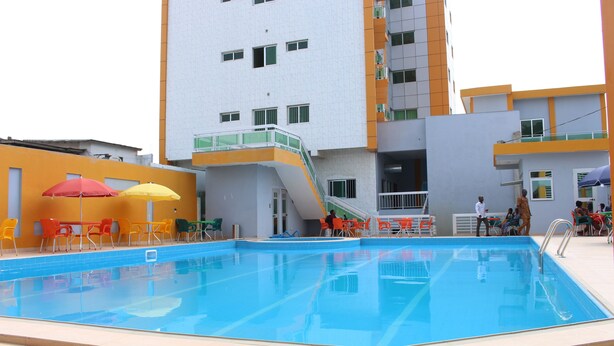 Una piscina con asientos exteriores cercanos y un edificio de varios pisos con balcones.