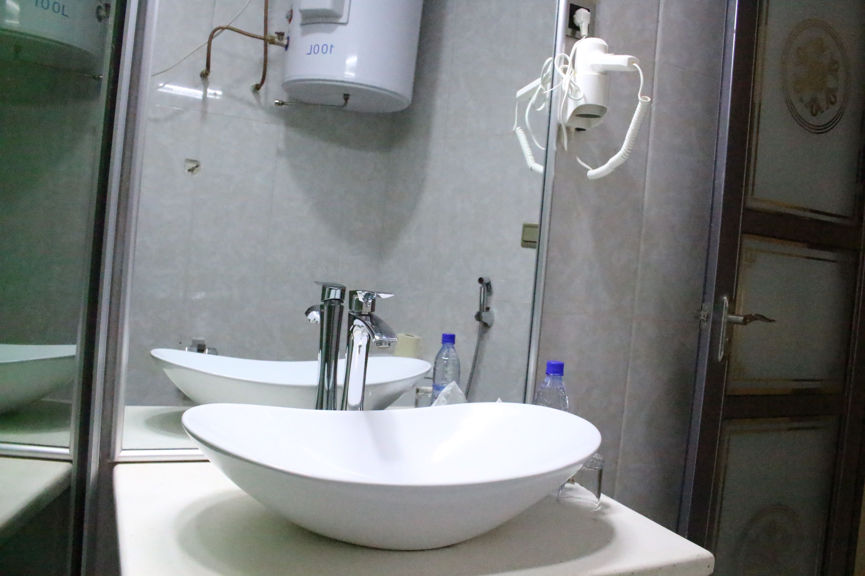 A bathroom with a large white sink, a mirror, and a white toilet. There is a towel dispenser and a soap dispenser on the wall.