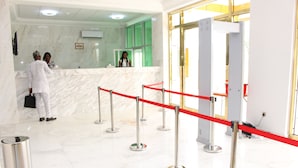 Zona de recepción de un hotel con suelo de mármol, mostrador de recepción y una barrera de cuerda roja.