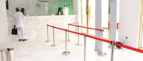 Zona de recepción de un hotel con suelo de mármol, mostrador de recepción y una barrera de cuerda roja.