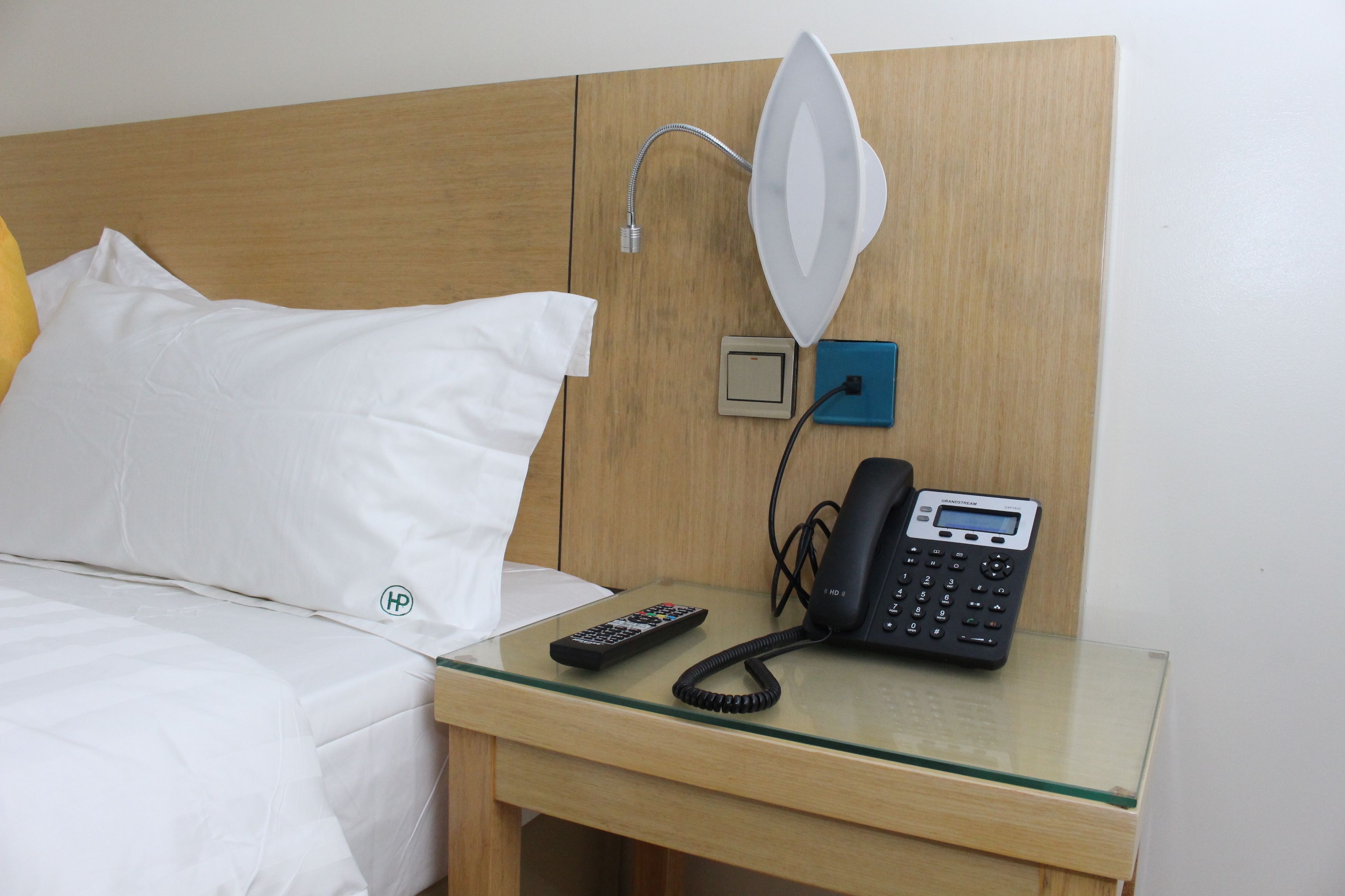 Habitación de hotel con cama, mesita de noche con lámpara, teléfono y control remoto.