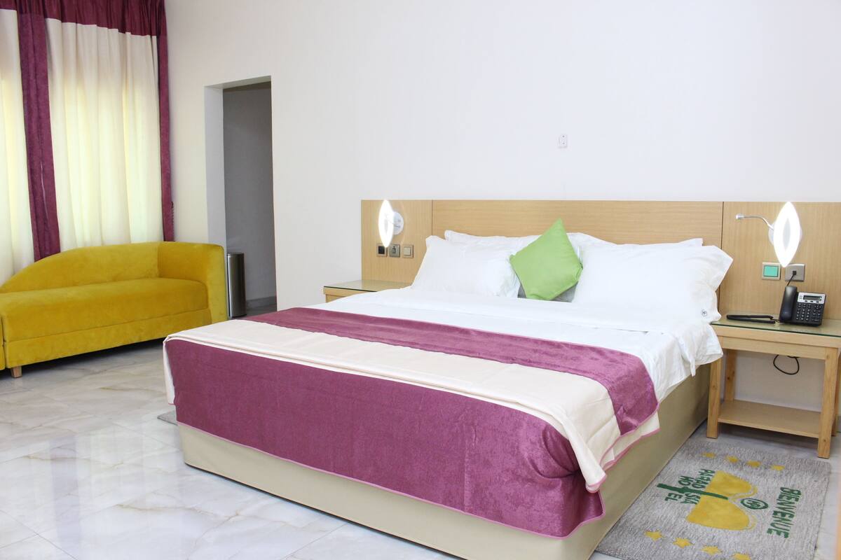 A hotel room with a bed, a nightstand, a lamp, a chair, and a rug.