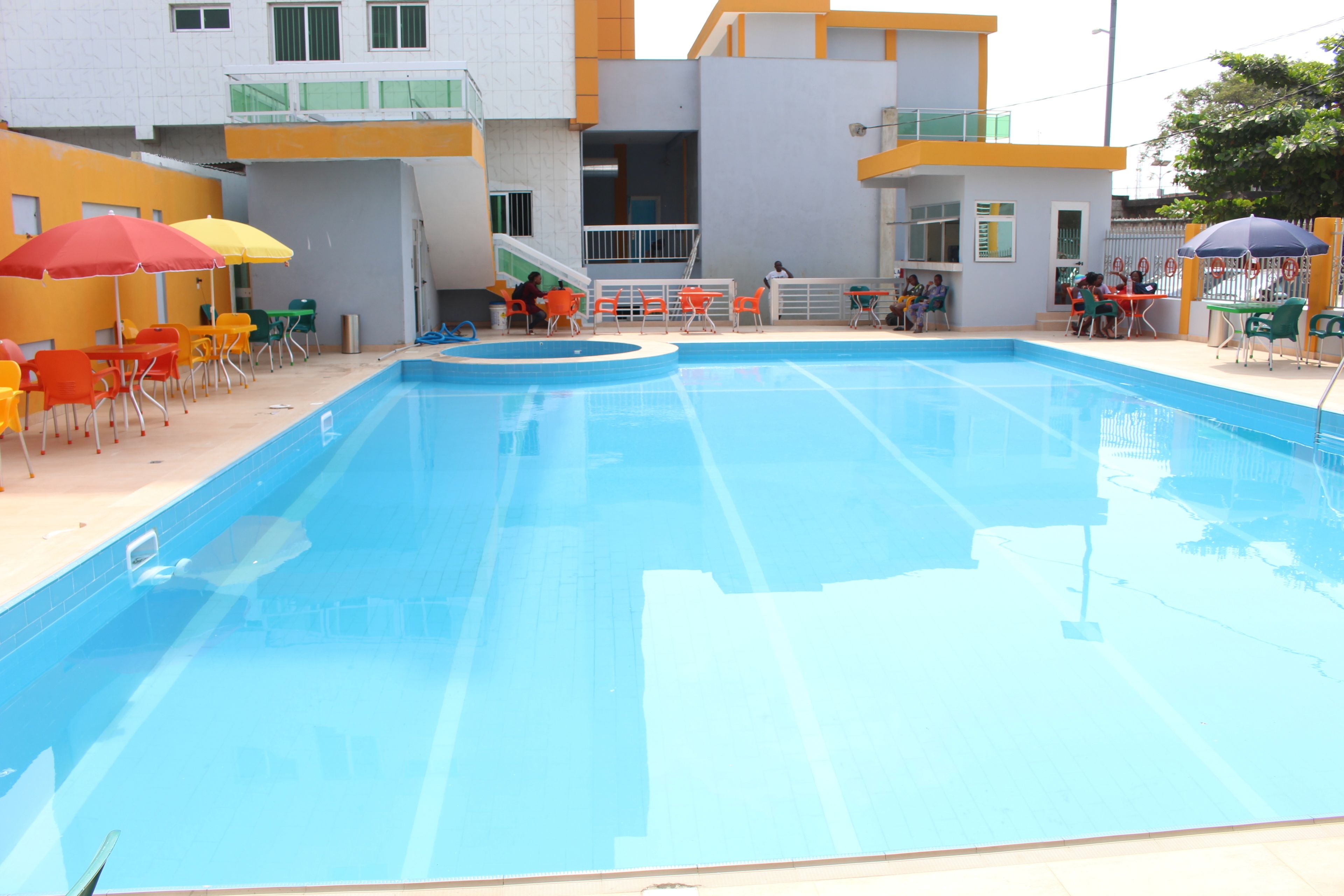 A swimming pool with a clear blue water surface, surrounded by outdoor seating areas with colorful chairs and umbrellas.