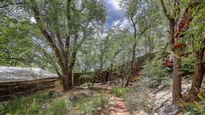 Un chalet rustique en bois, entouré d’une forêt dense et accessible par un sentier pavé de pierres.